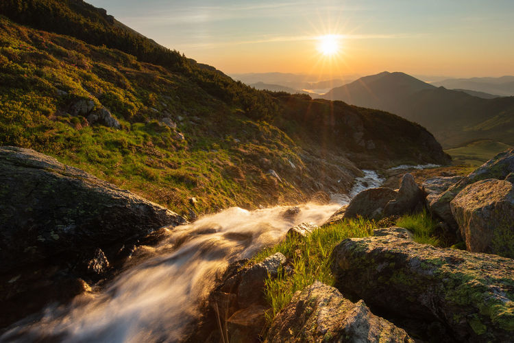 Scenic view of stream amidst rocks against sky during sunrise in rodnei mountains 