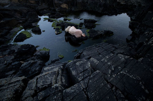 Naked woman on rock by lake against sky