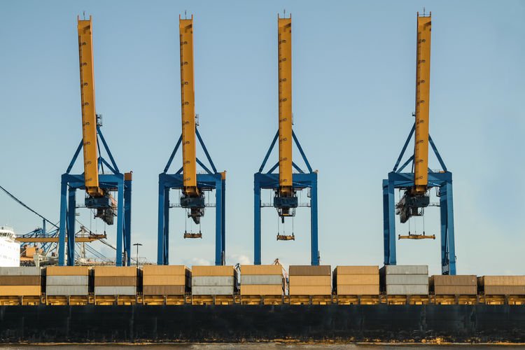 Commercial cranes in dock against clear sky