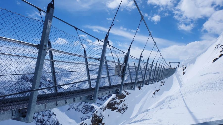 Footbridge on snowcapped mountain against cloudy sky