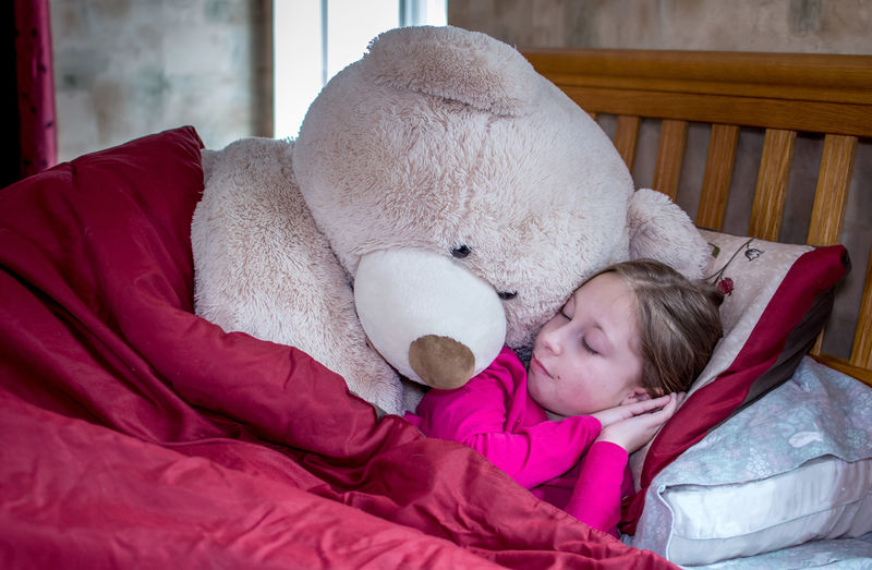 Cute little girl in bed with a giant teddy bear. someone is snoring