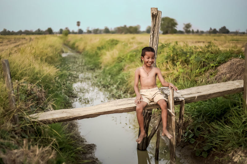 Smiling boy sitting on wood over canal at farm