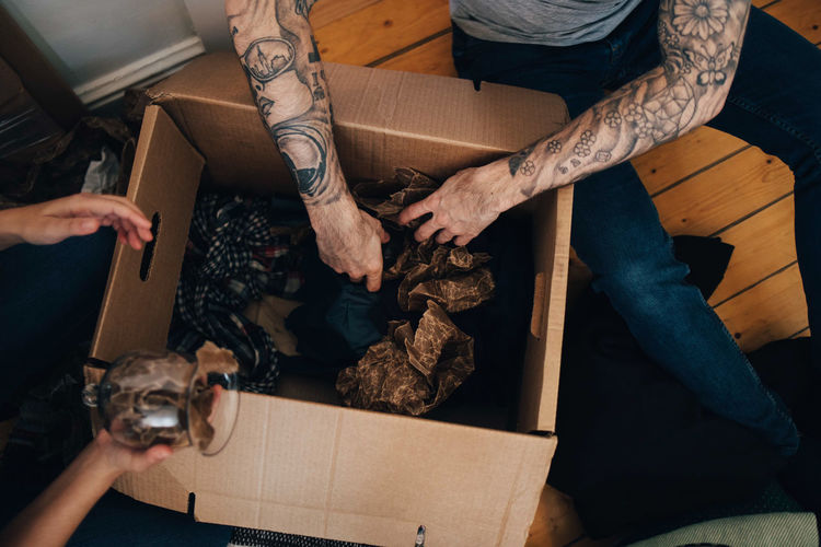 Cropped image of couple unpacking cardboard box while sitting on floor at home