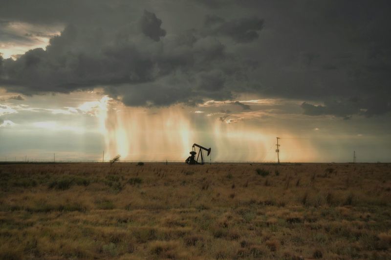 Mid distance view of oil well on field against cloudy sky during sunset
