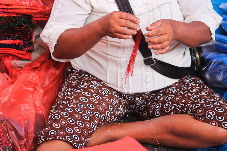 Midsection of woman holding tassel while sitting amidst clothes