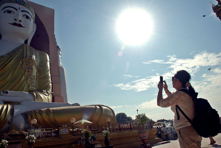 Woman photographing buddha statue against sky 