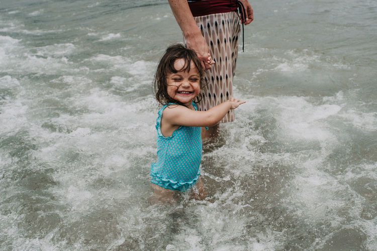 Cheerful daughter holding mother hand while playing in sea
