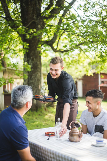 Smiling young waiter talking with customers while working at outdoor cafe