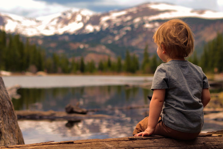 Rear view of boy looking at lake against mountain range