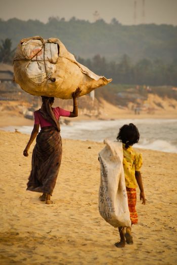 Rear view of woman and girl carrying burlap sacks