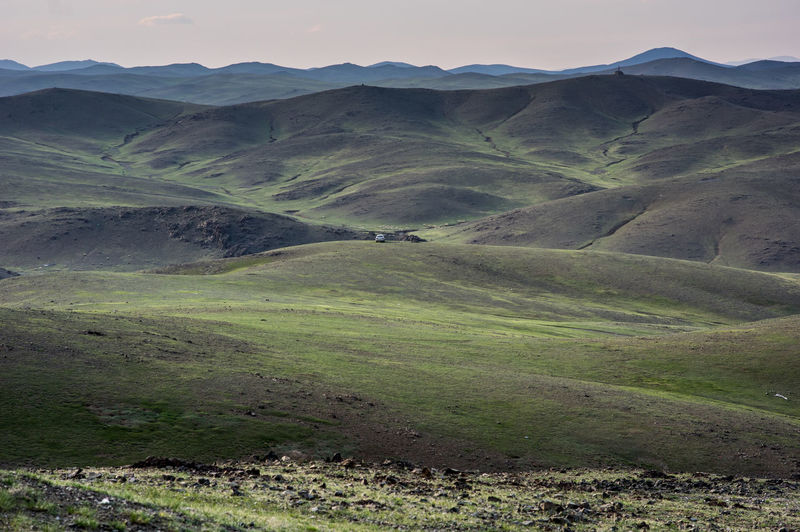 A single car parked hillside in mongolias vast landscape amid lush green hills.
