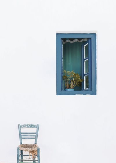 Potted plant against white wall, blue chair  in serifos, cyclades, greece 