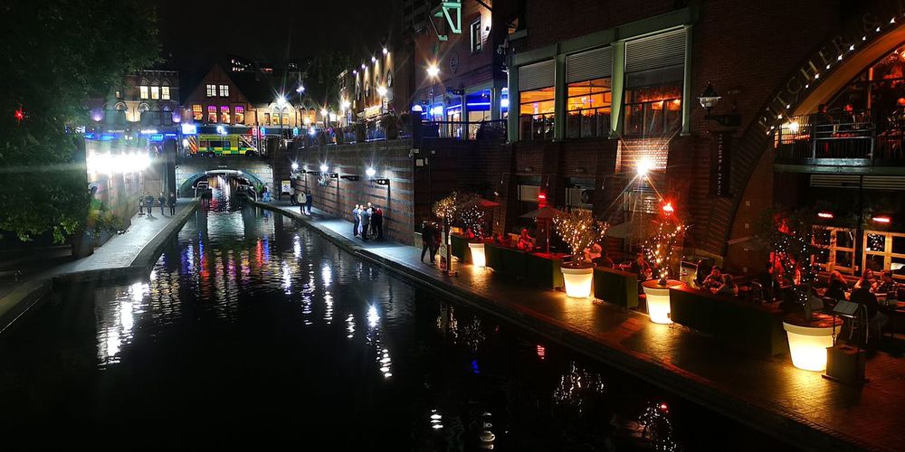 Illuminated street by canal in city at night