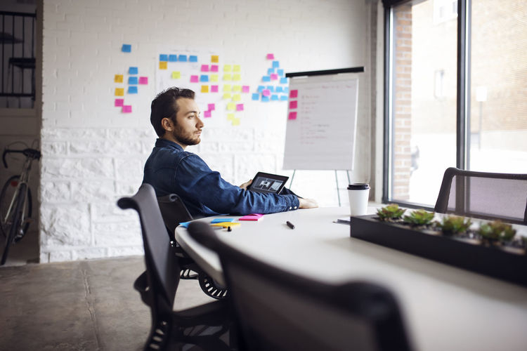 Thoughtful businessman using tablet while sitting on chair in office