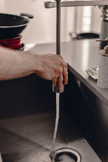Cropped hand of man washing sink in home