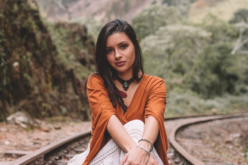 Portrait of beautiful young woman sitting on railroad tracks
