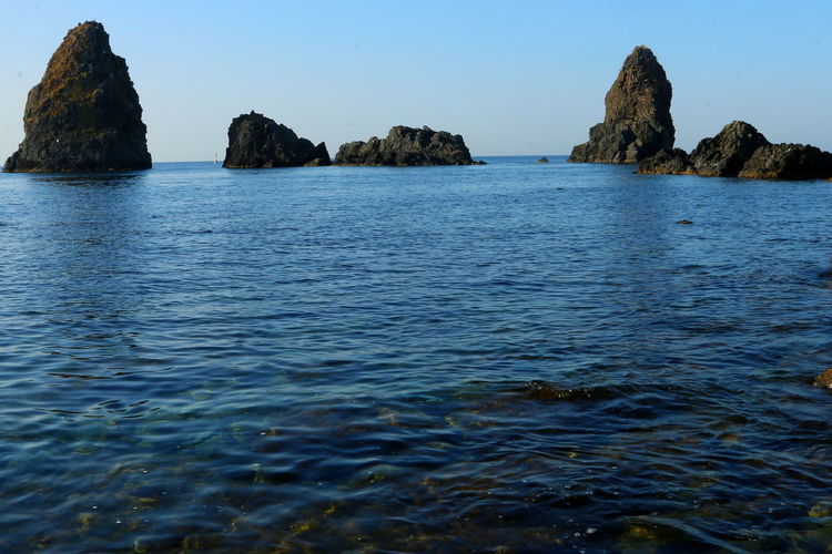 Scenic view of rock formations in sea against clear blue sky