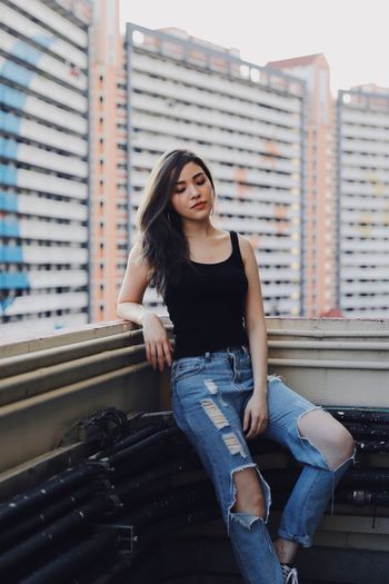 Young woman wearing torn jeans standing against building in balcony