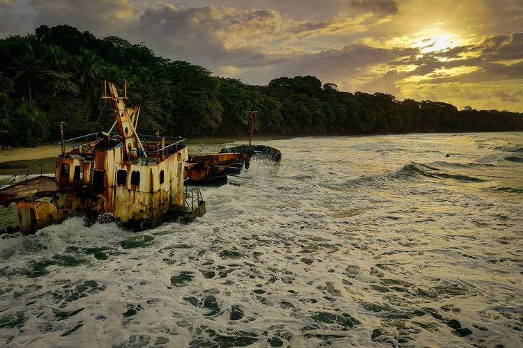 Scenic view of beach against boat during sunset