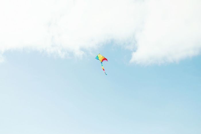 Low angle view of multi colored kite flying against cloudy sky