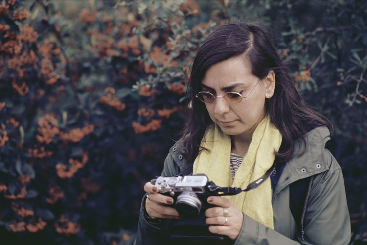 Close-up of woman holding camera against trees in forest