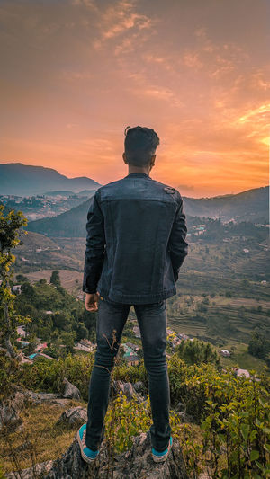 Rear view of man looking at mountains against sky during sunset