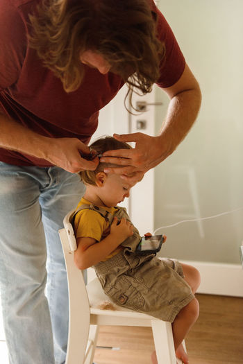 Dad cutting hair to little son at home