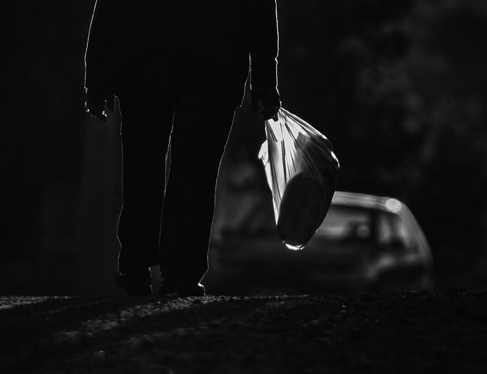 Low section of person holding plastic bag while walking on road at dusk