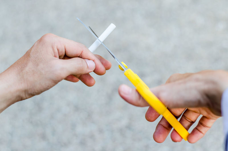 Cropped hands of man cutting cigarette with scissors 