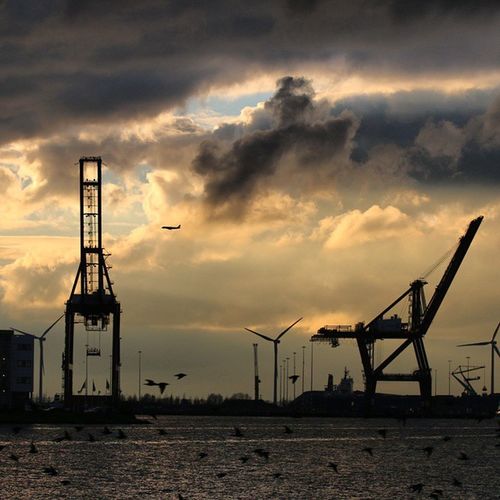 Crane at harbor against cloudy sky