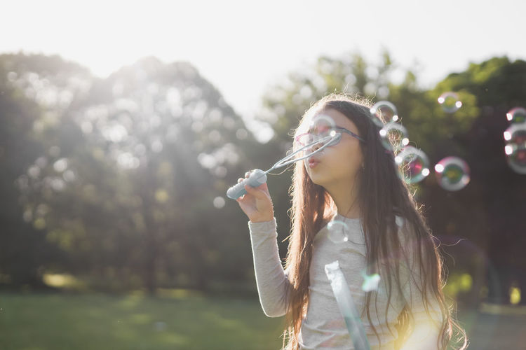 Portrait of a beautiful caucasian girl blowing soap bubbles in a meadow in a park