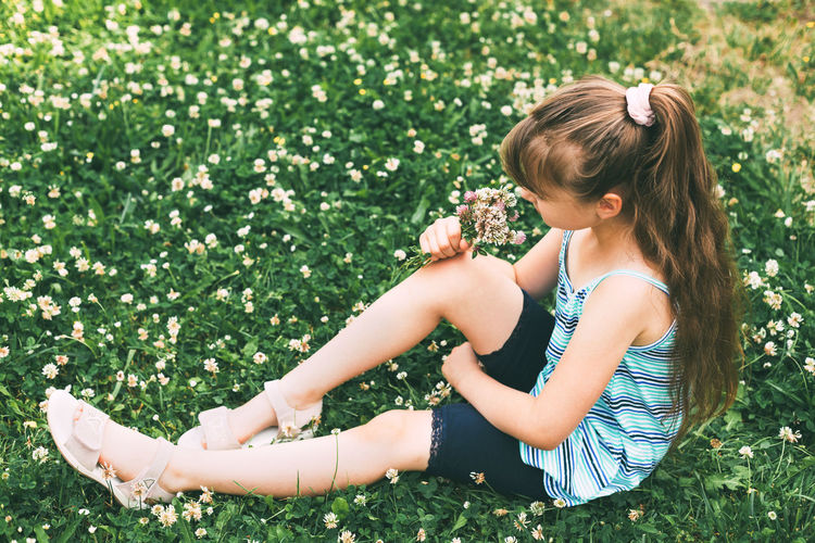 A cute caucasian girl is sitting in a clover meadow and collecting a bouquet. rest from the city. 