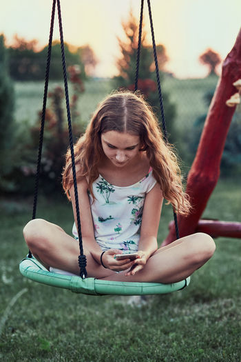 Girl using mobile phone while sitting on swing
