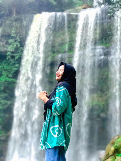 Smiling woman in hijab standing against waterfall