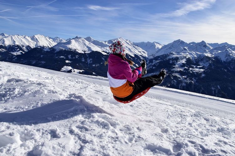 Girl tobogganing on ski slope against sky