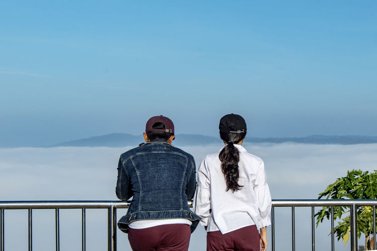 Rear view of couple standing by railing against sky