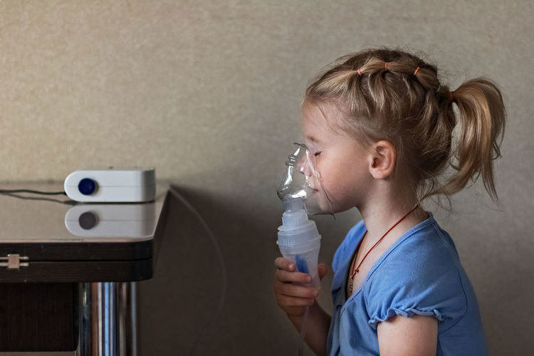 Side view of girl breathing with nebulizer at home
