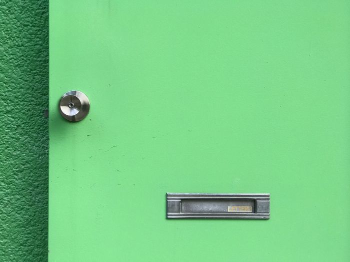 Close-up of closed green door with mail slot