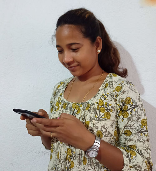 Young woman using mobile phone against wall