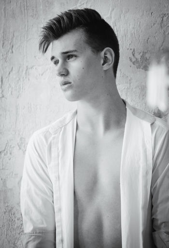 Young man looking away while standing against wall
