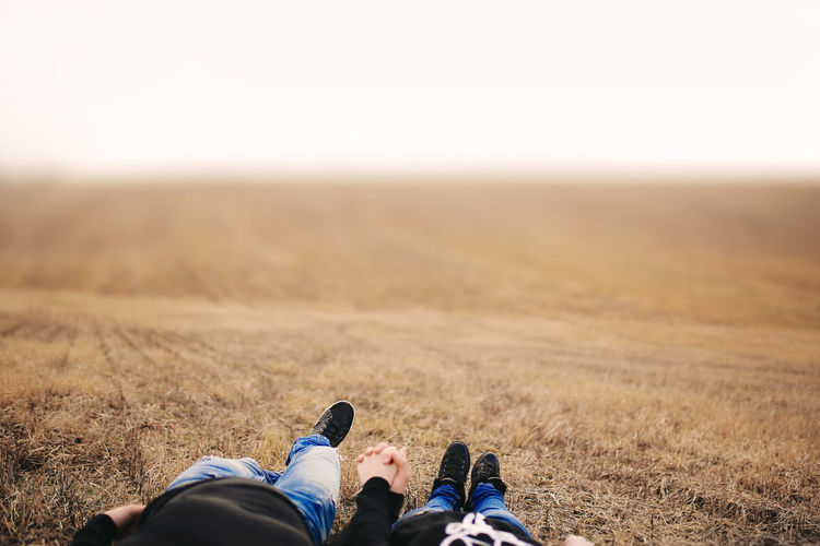 Low section of couple holding hands while relaxing at field