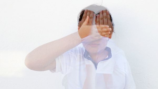 Double exposure of boy covering face against white background