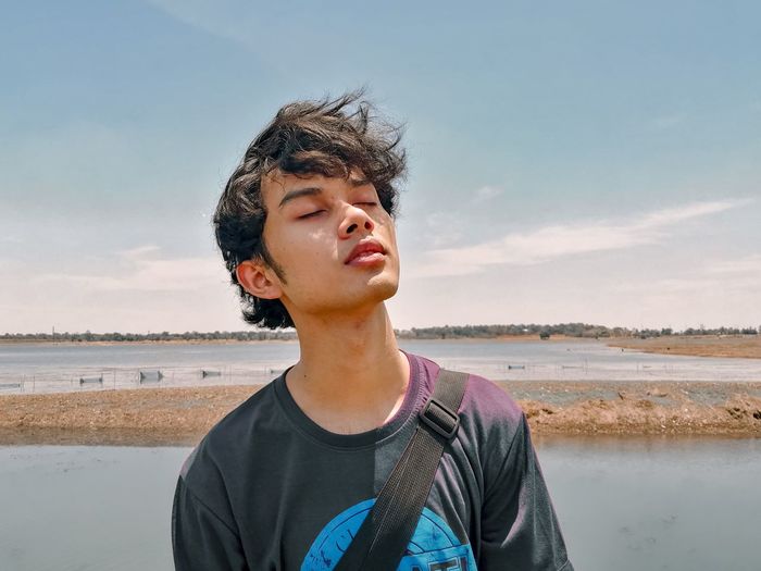 Portrait of teenage boy closing his eyes against sky