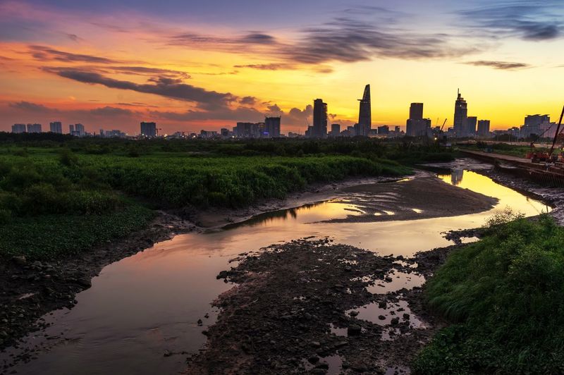 Scenic view of river by cityscape against sky during sunset