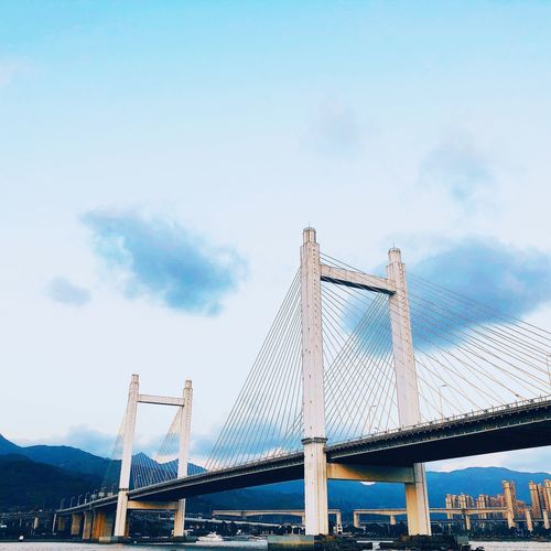 Low angle view of suspension bridge against cloudy sky