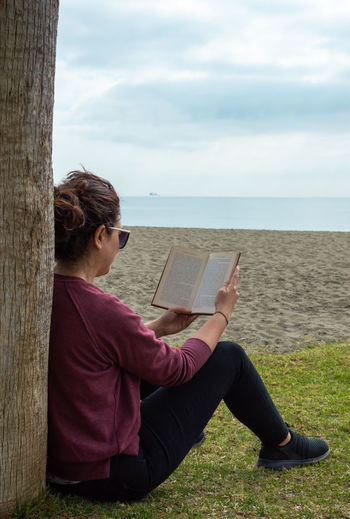 Woman sitting on book by sea against sky
