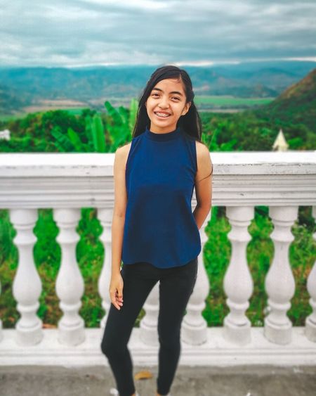 Portrait of smiling teenage girl standing at observation point against landscape