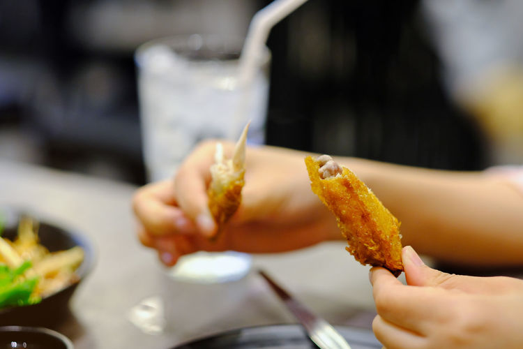 Close-up of woman holding fried chicken wing at restaurant table