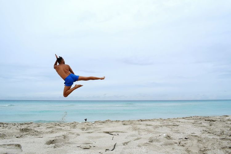 Shirtless man jumping on beach against sky