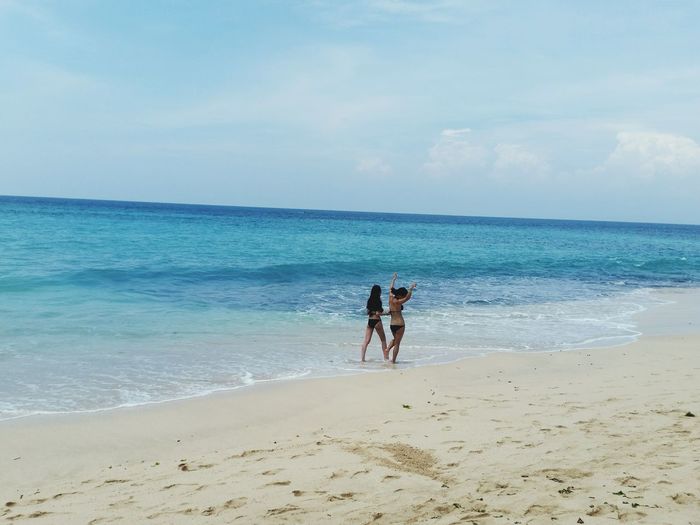 Rear view of women wearing bikini at beach against sky